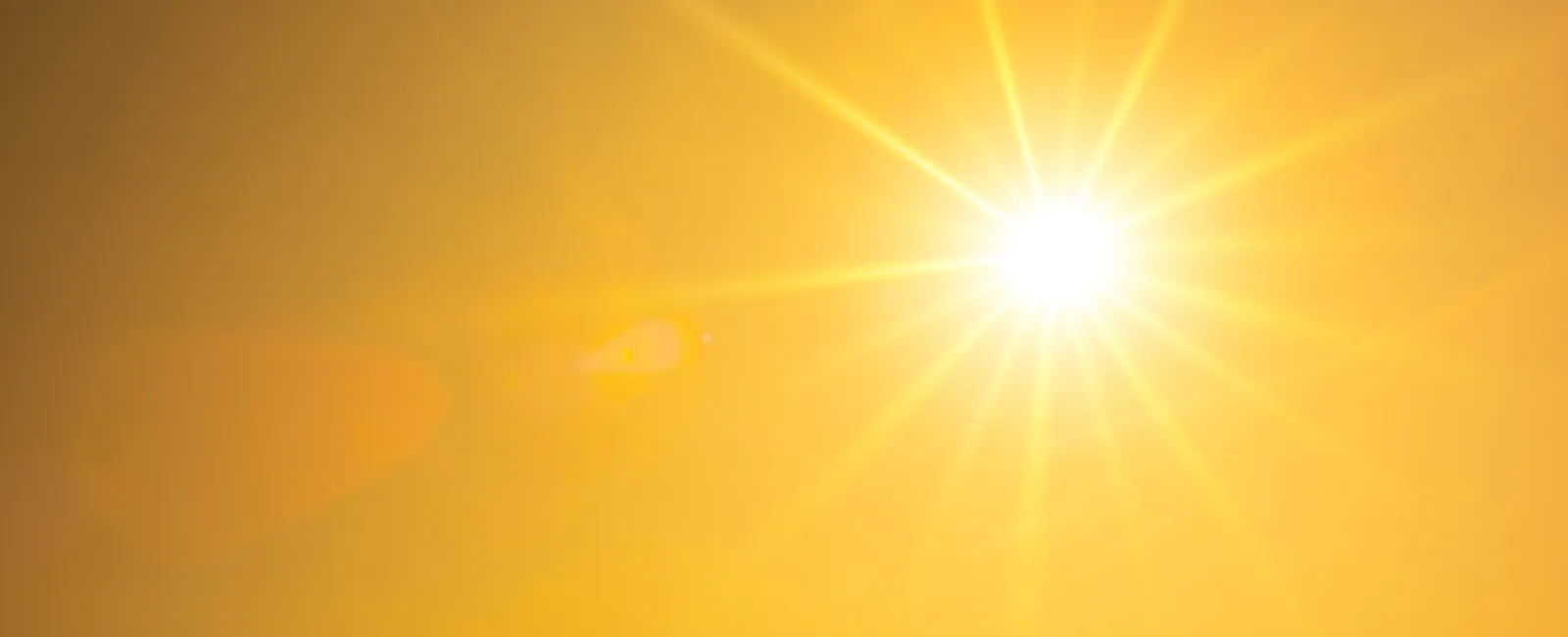 Bright sun with radiant beams shining in a clear yellow-orange sky, evoking warmth and daylight.