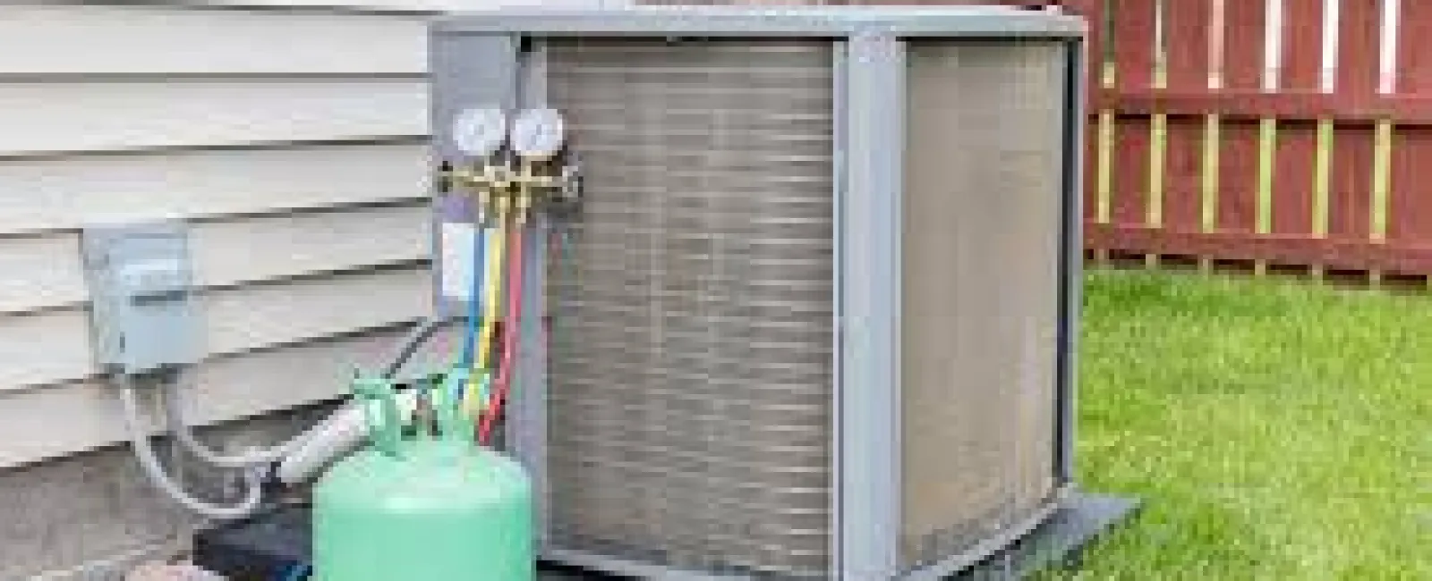 Residential HVAC unit installed outside a house with refrigerant tank and pressure gauges on green lawn.