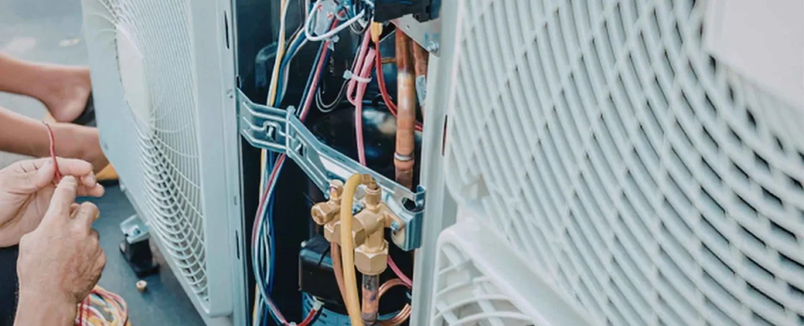 Technician repairing and wiring components inside an outdoor air conditioning unit with visible copper pipes and wires.