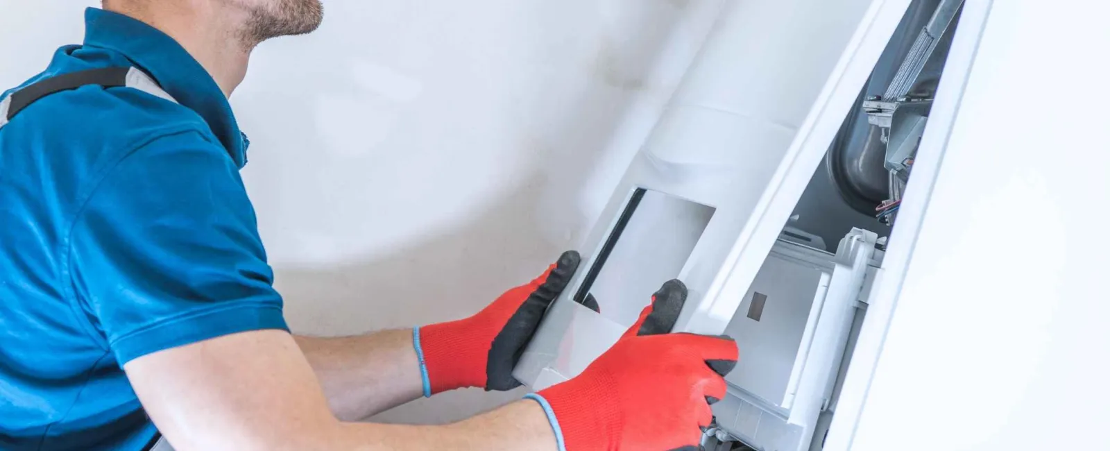 Technician wearing red gloves repairing or installing a white boiler or HVAC unit on a wall indoors.