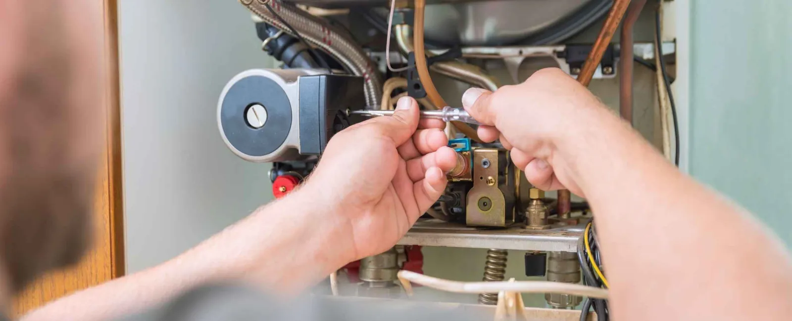 Technician using a wrench to repair or maintain an open boiler or furnace with visible pipes and wiring.