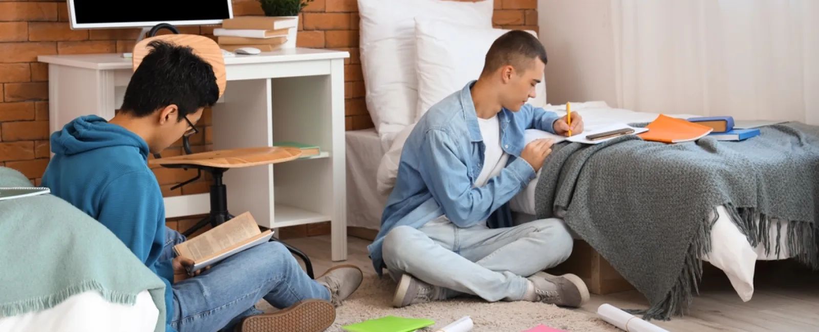 Two students studying with books and notebooks while sitting on the floor in a cozy bedroom