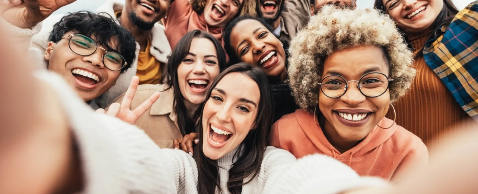 Diverse group of happy young adults taking a cheerful selfie outdoors, smiling and enjoying together.