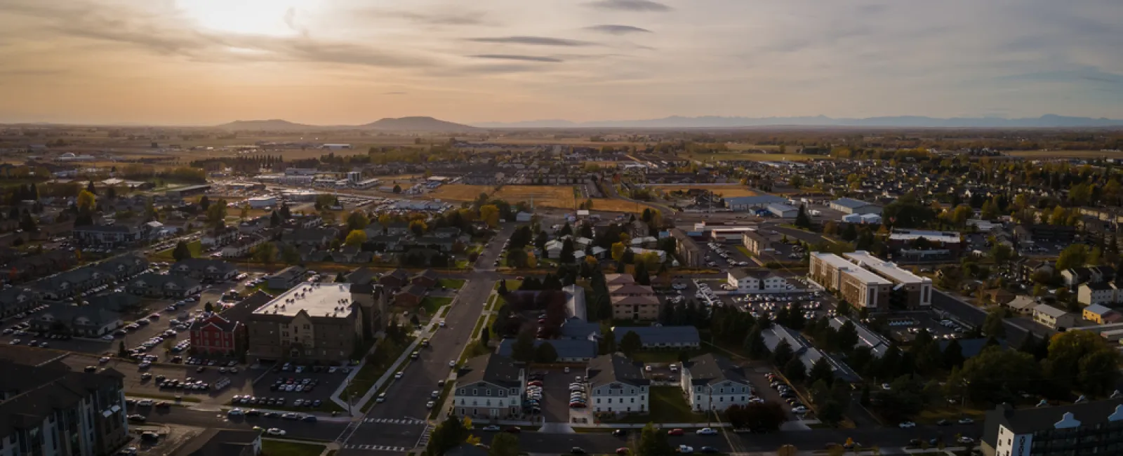Aerial view of a suburban town at sunset with roads, houses, and distant mountains under a cloudy sky