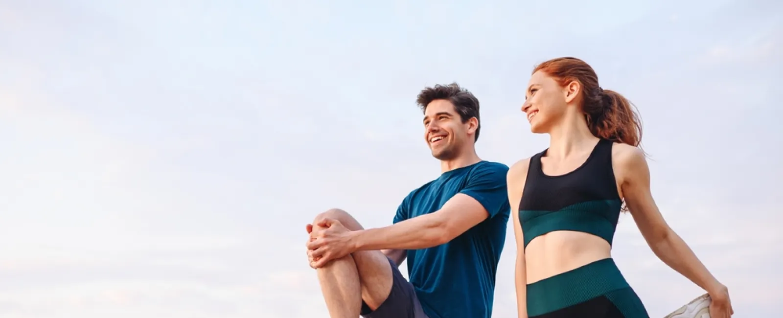 Young man and woman stretching by the sea, preparing for workout during early morning or evening.