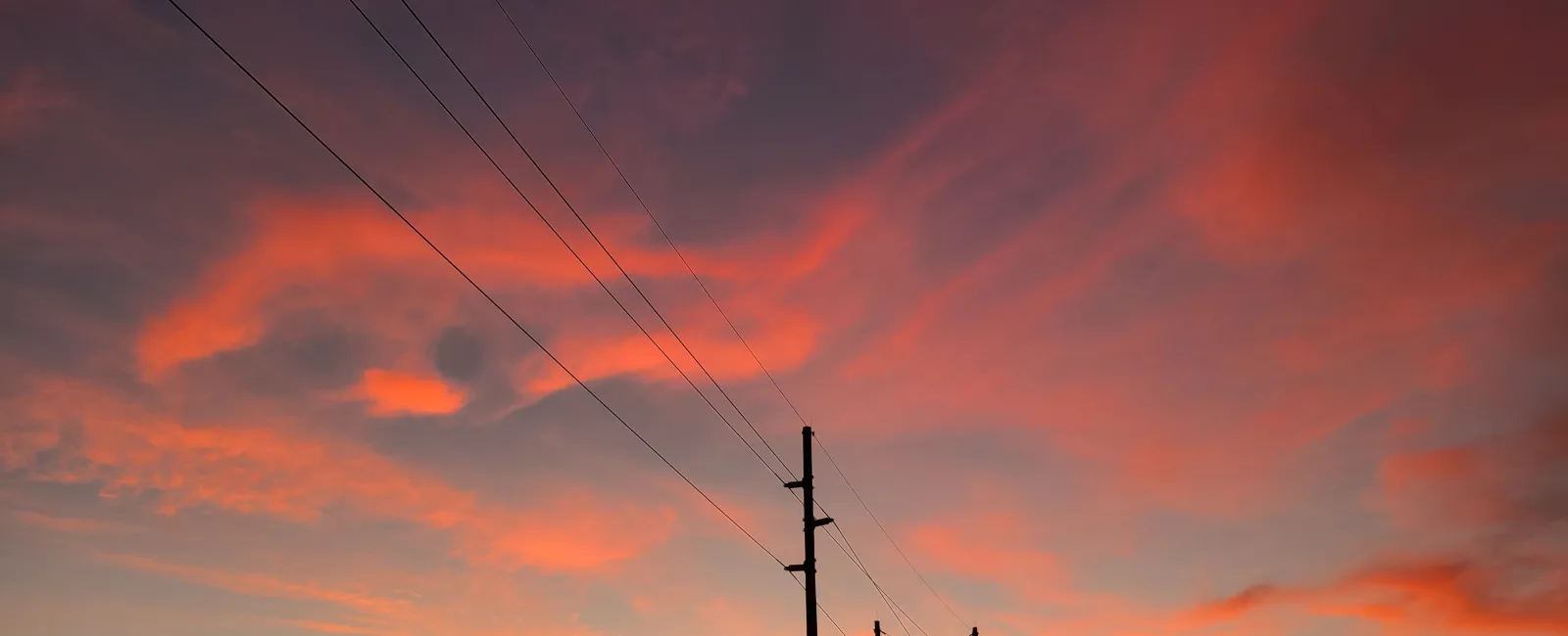 Sunset with vibrant orange and purple clouds behind silhouetted power poles and lines.