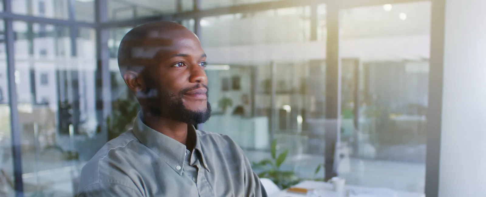 Confident young black man standing with arms crossed in bright modern office space with glass walls.