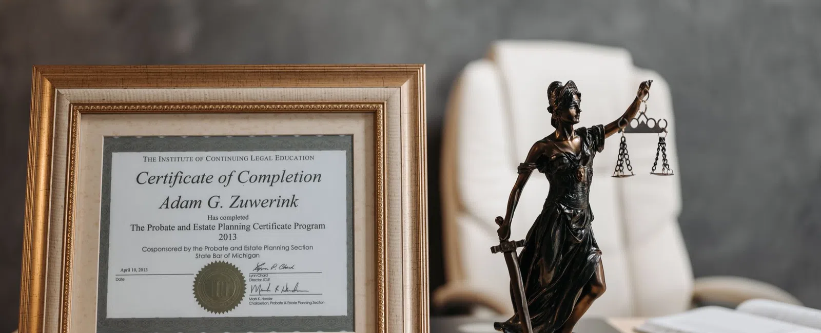 Framed legal certificate and bronze Lady Justice statue on desk with office chair and book in background