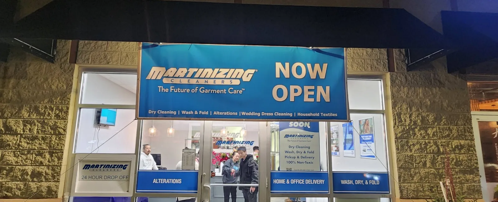 Martinizing Cleaners storefront at night with blue signage announcing now open and service details.