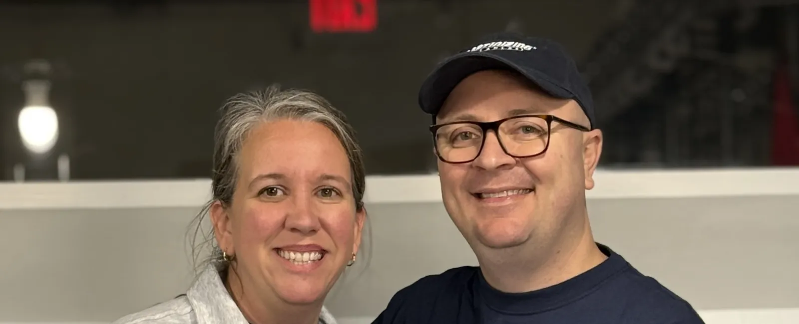 Smiling man and woman wearing matching cleaning service uniforms standing behind a counter indoors.