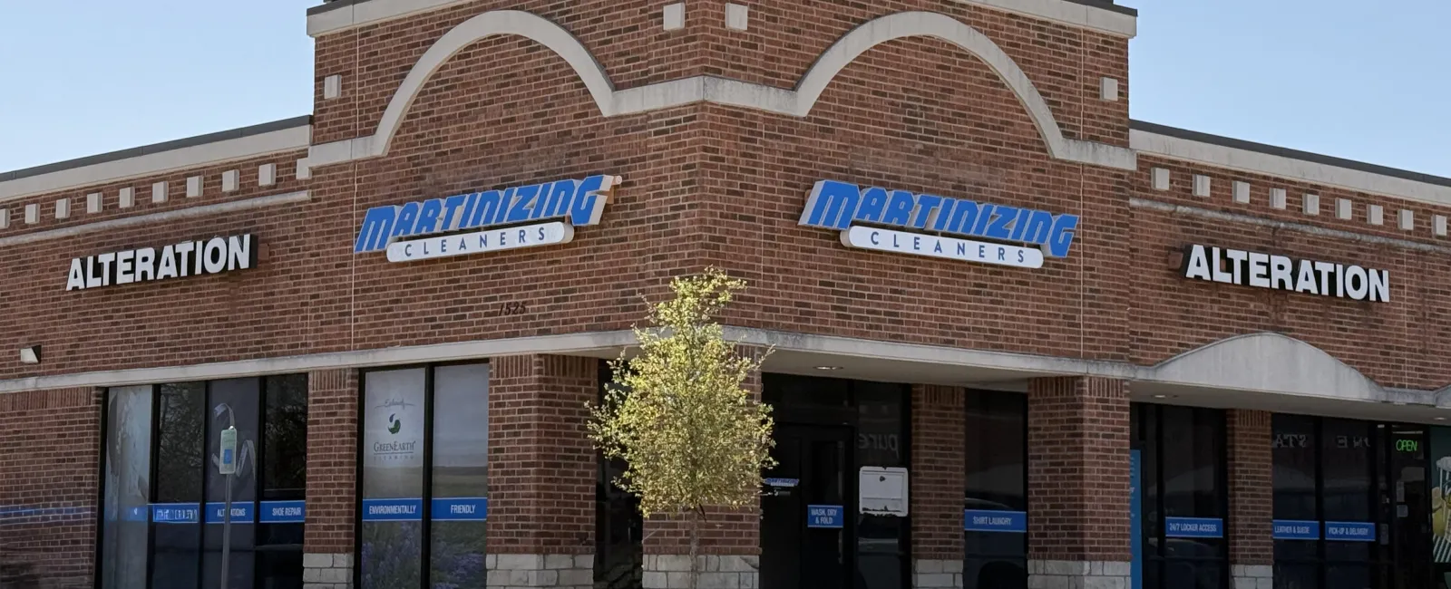 Brick corner storefront of Martinizing Cleaners offering alteration services under clear blue sky.