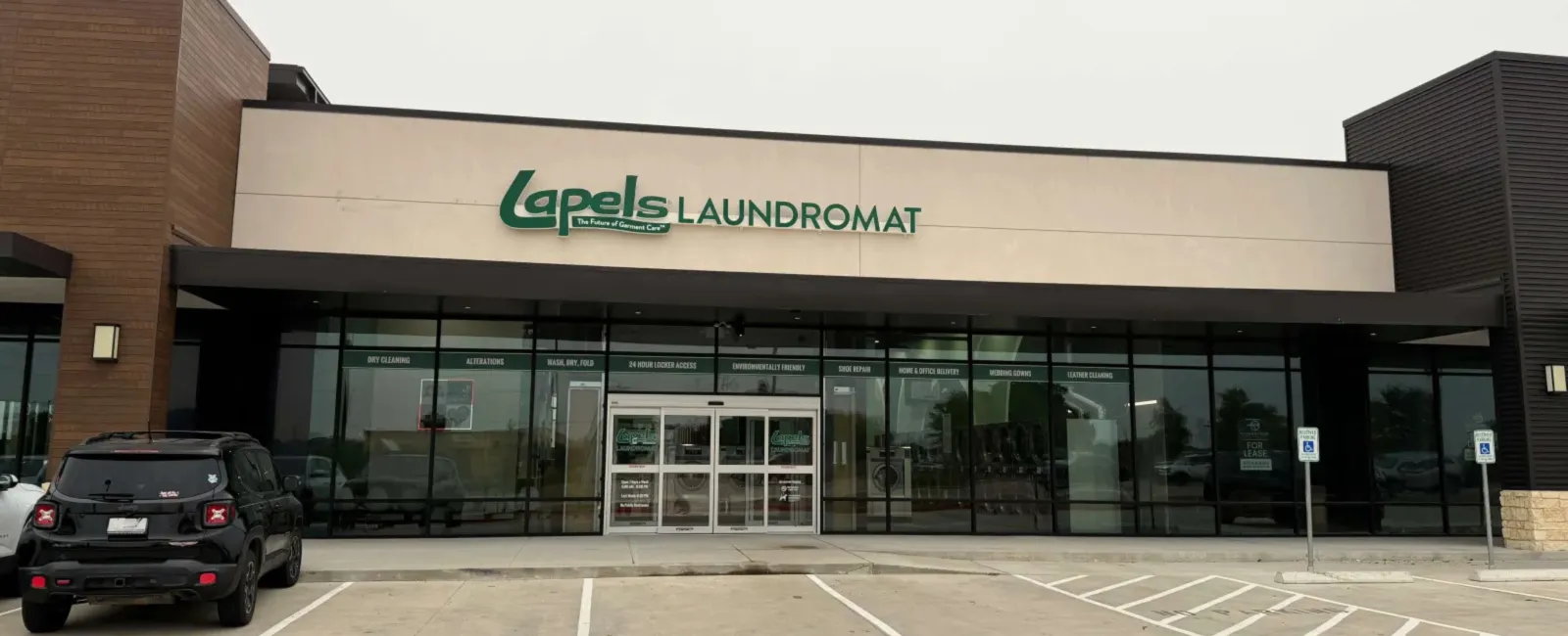 Exterior view of a Lapels Laundromat storefront with parking spaces and a black SUV outside.