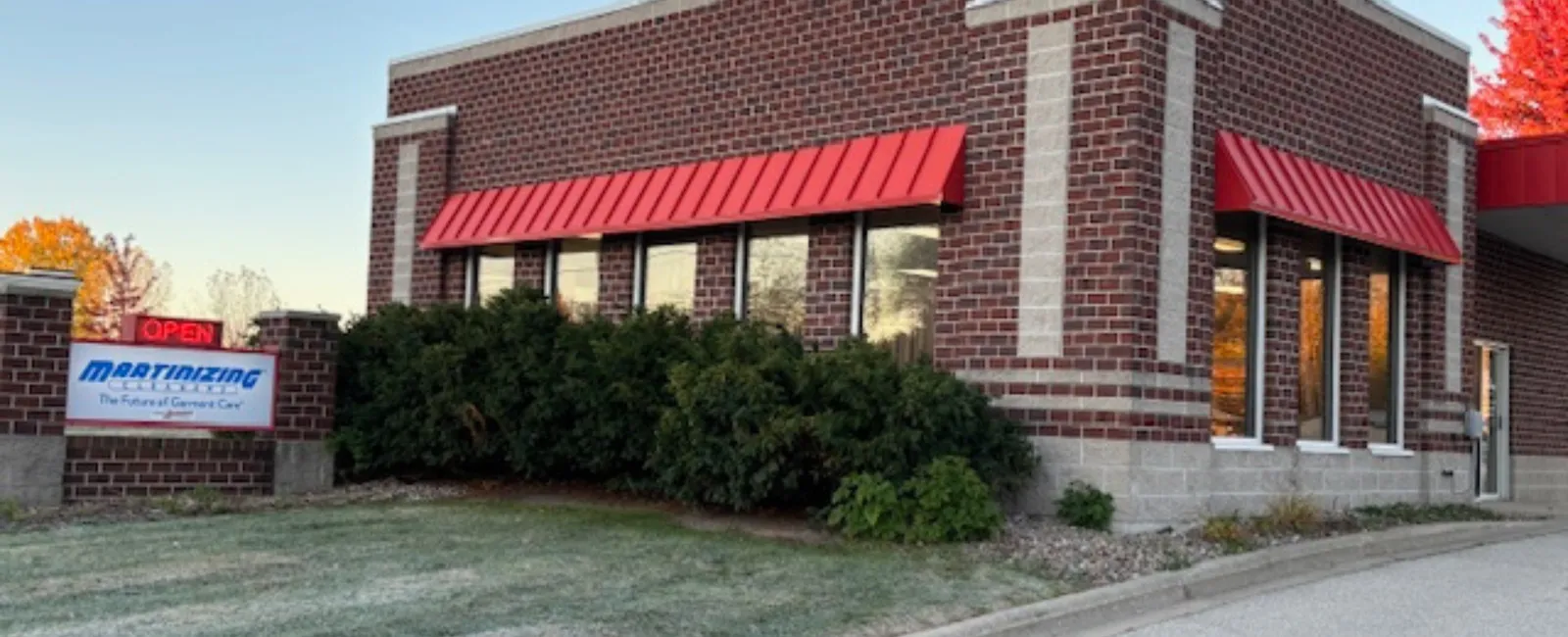 Brick commercial building with red awnings and a sign for Martinizing Dry Cleaning at dusk with trees in background