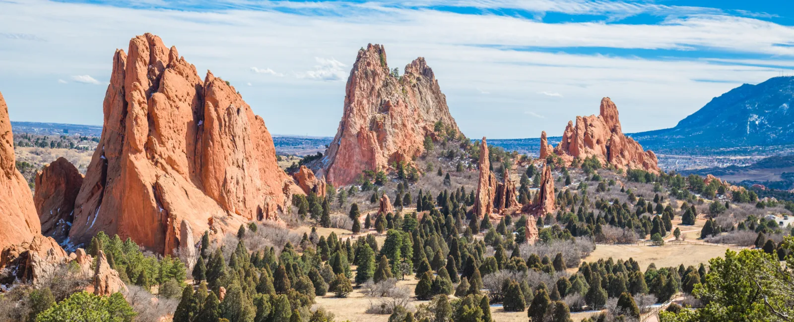 Red sandstone rock formations rise above green pine trees under a blue sky at Garden of the Gods park.