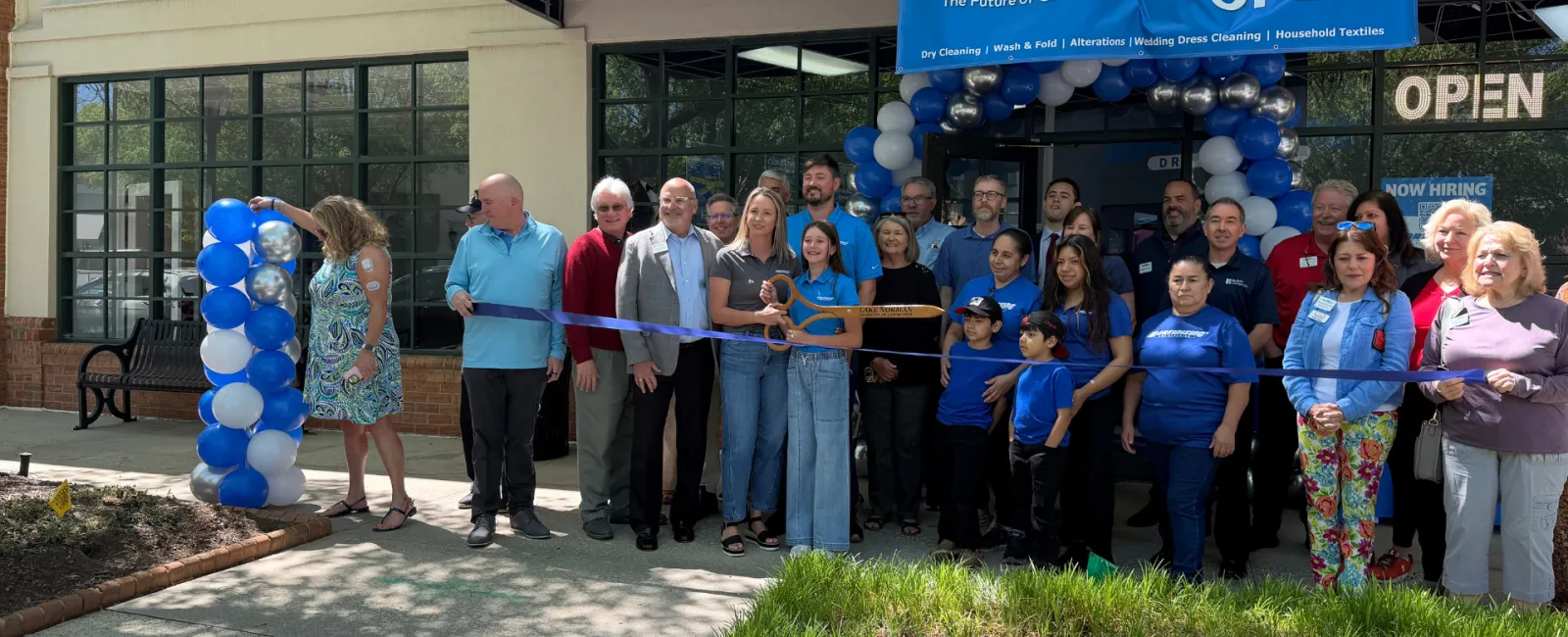 Group of people at a ribbon-cutting ceremony for Martinez Cleaners new store opening with blue and white balloons.