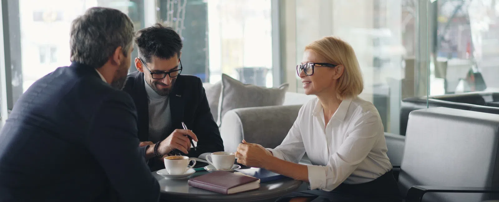 Three professionals having a business meeting over coffee in a modern cafe with notebooks and tablets.