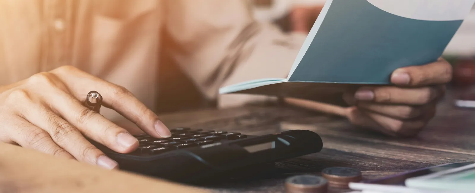 Person using calculator and holding checkbook at table trying to save money on IT expenses