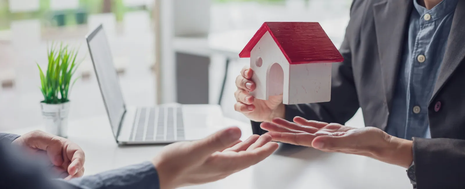 Real estate agent handing over a small house model to a client - Computer in background needing IT services