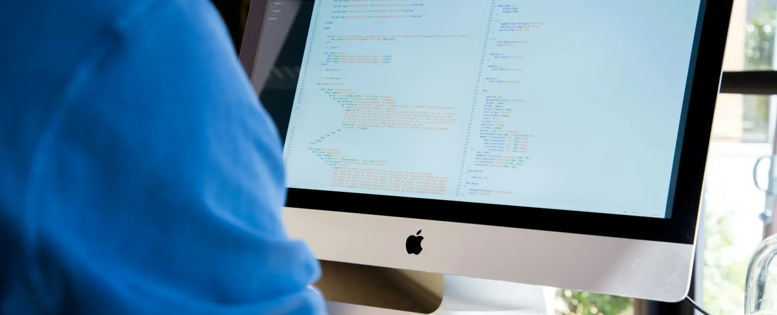 Person coding on an Apple iMac computer displaying programming code on highlighting the usefulness of local IT.