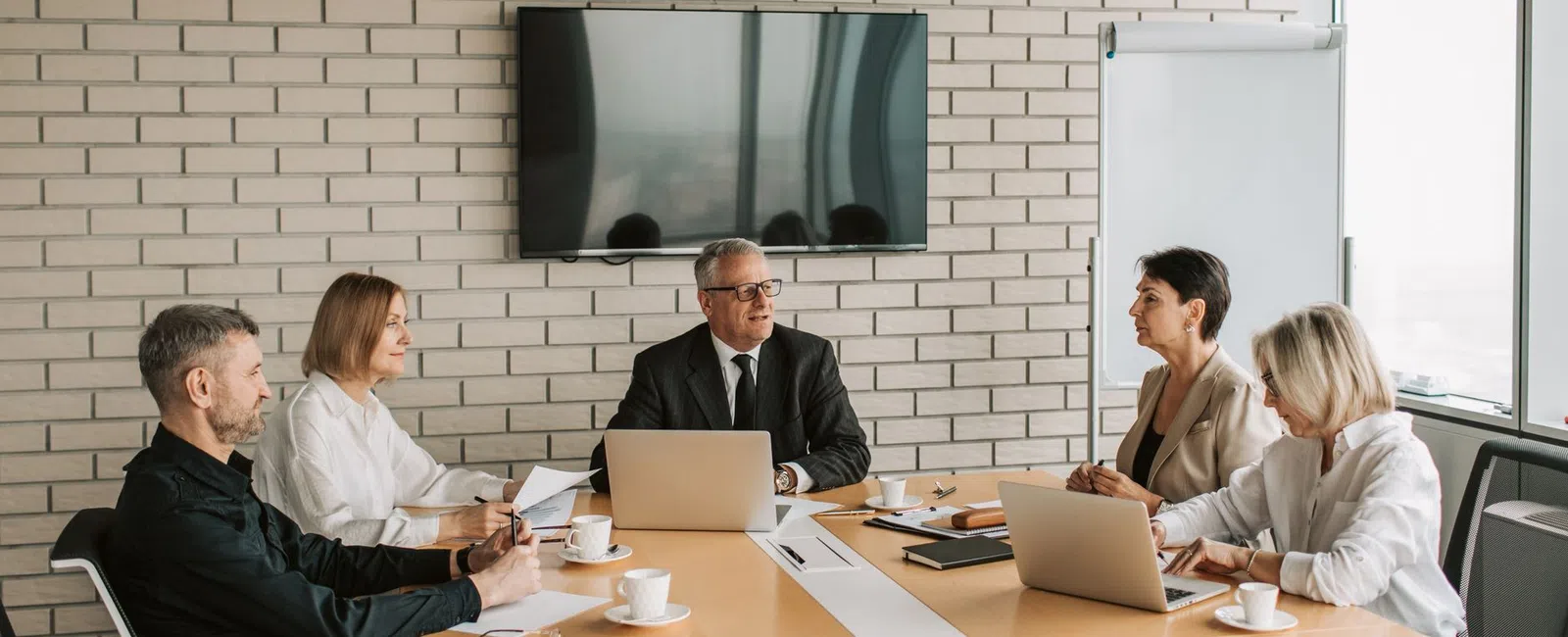 Business team of five in formal attire having a meeting in a modern office conference room.