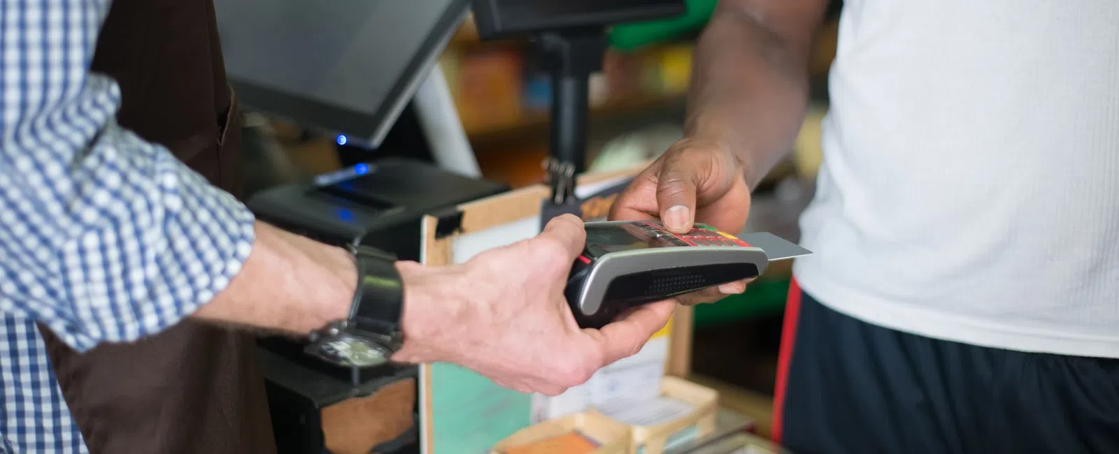 Customer making contactless payment with card at store checkout counter held by cashier