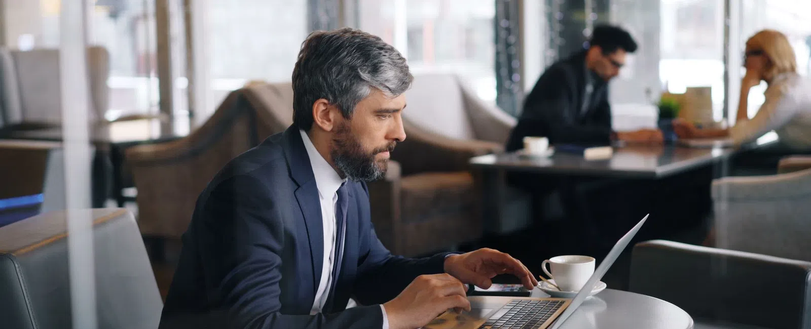 Man in suit working on laptop at cafe table with coffee cup, focused and professional environment.