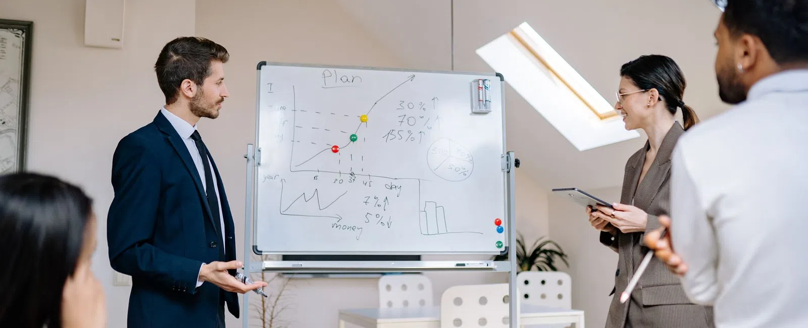 Business team discussing growth plans with charts on whiteboard in modern office with natural light.