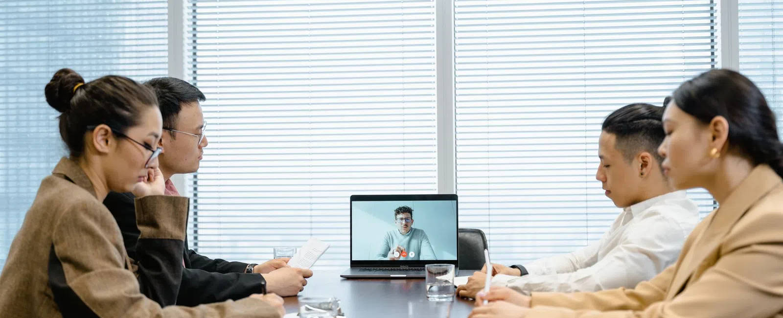 Four people in a meeting room engaged in a video conference with a person on a laptop screen.