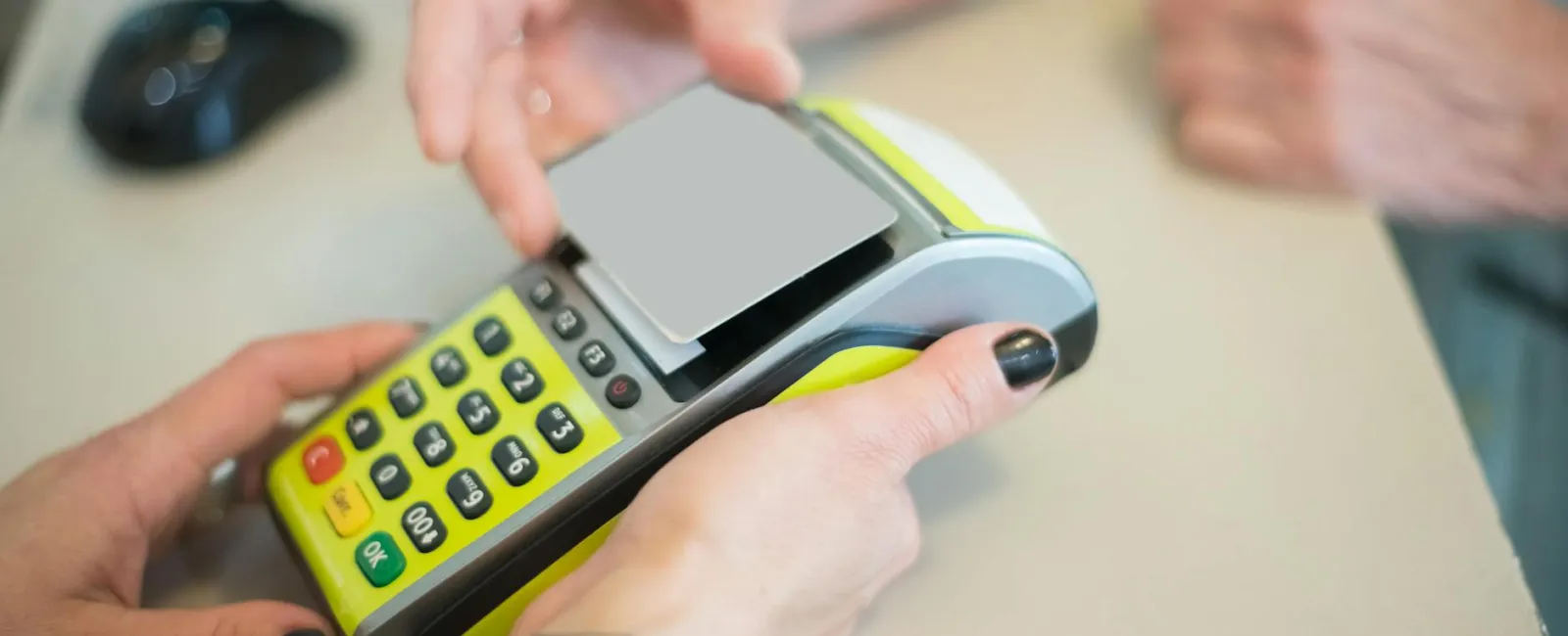 Customer making a contactless payment with a card on a handheld card reader at a counter.