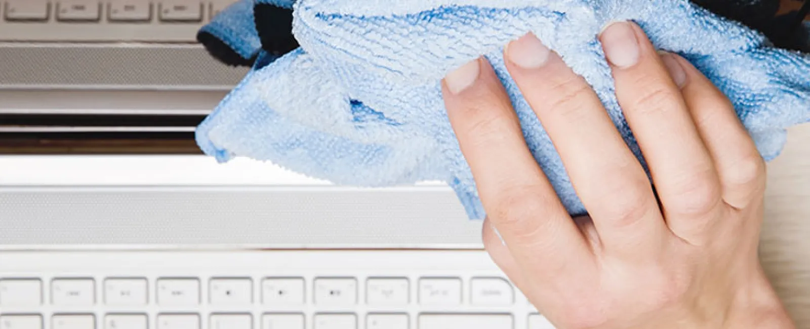 a person's hand holding a blue towel over a white laptop