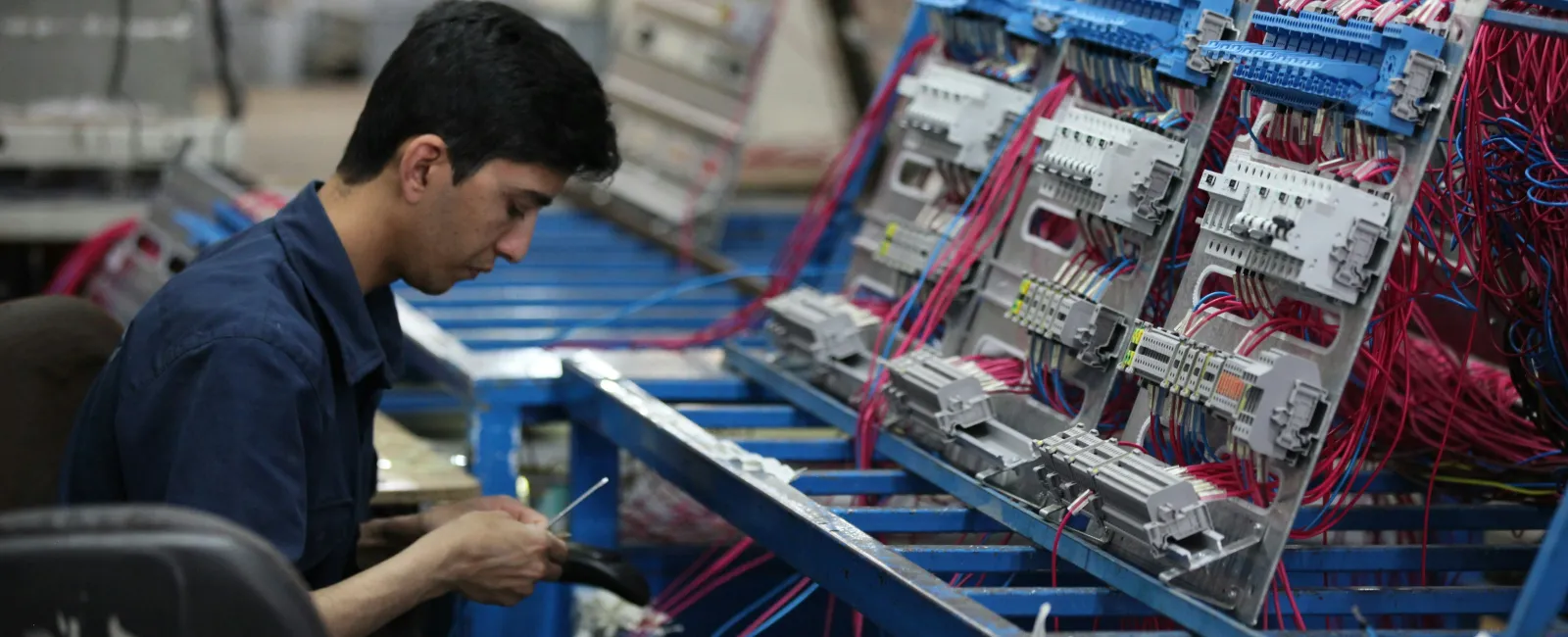 Technician assembling and wiring electrical control panels with organized cables in an industrial setting.