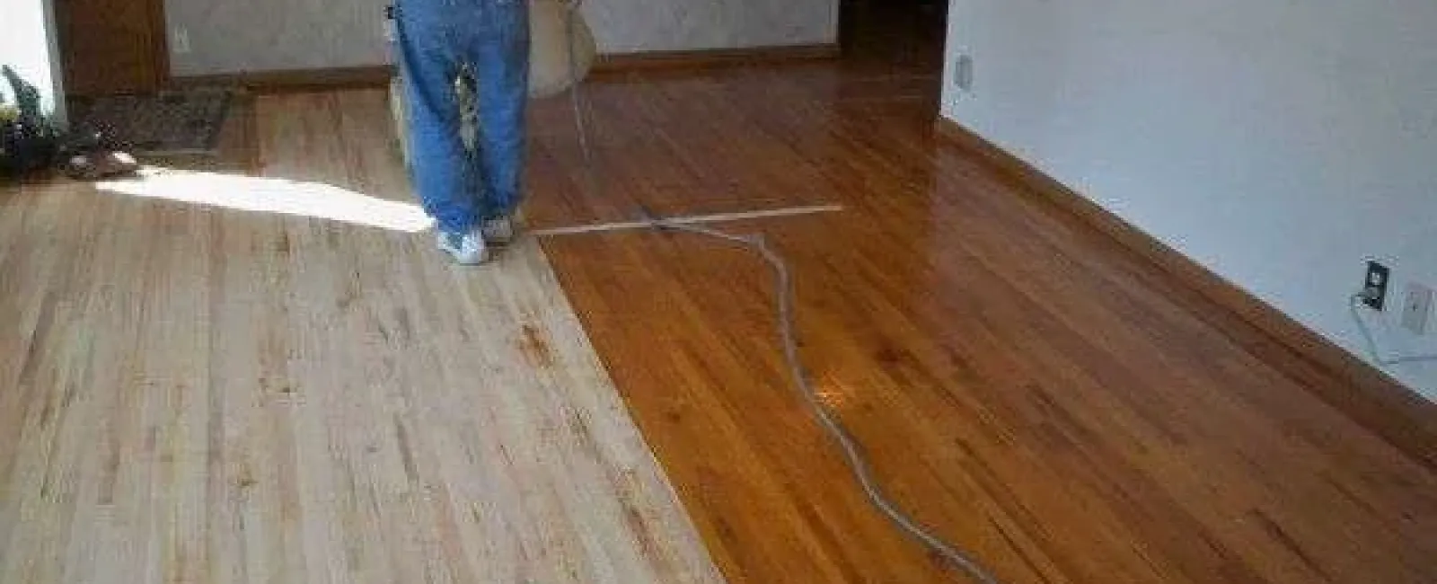 Person refinishing a hardwood floor showing contrast between sanded light wood and finished darker wood.
