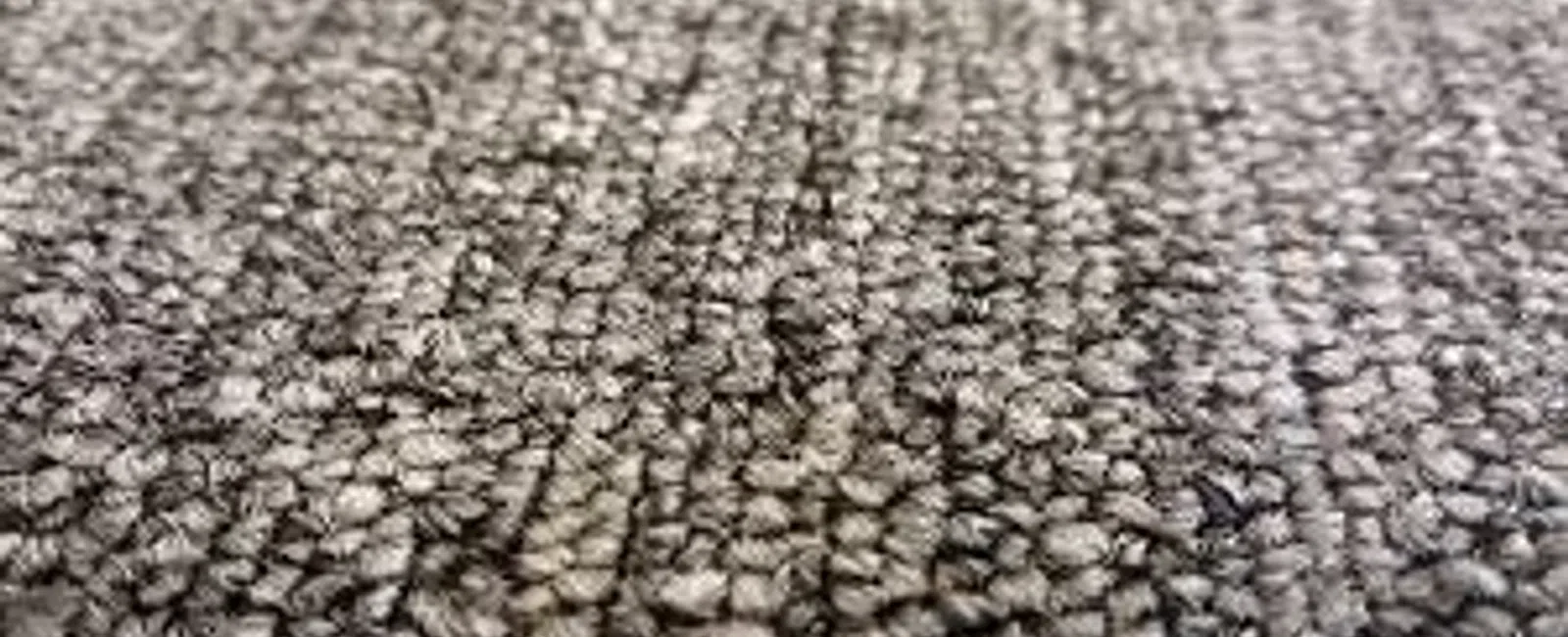 Close-up of gray textured carpet fibers showing detailed woven pattern and texture in soft lighting