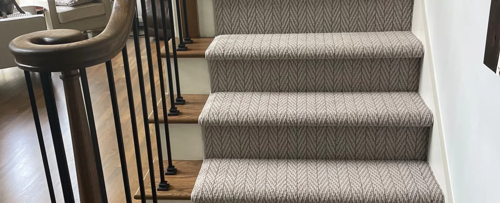 Indoor wooden staircase with patterned carpet runner and black metal balusters in a bright living room.