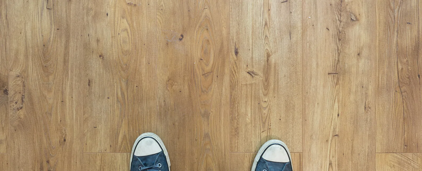 Top view of worn blue sneakers on a wooden floor with natural grain patterns and knots.
