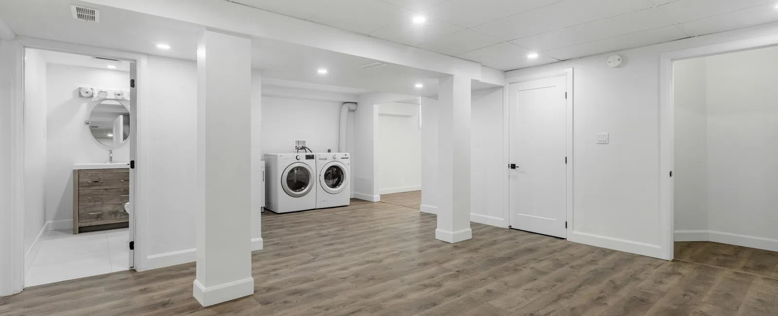 Spacious basement with wood flooring, white walls, washer and dryer, bathroom, and recessed ceiling lights.