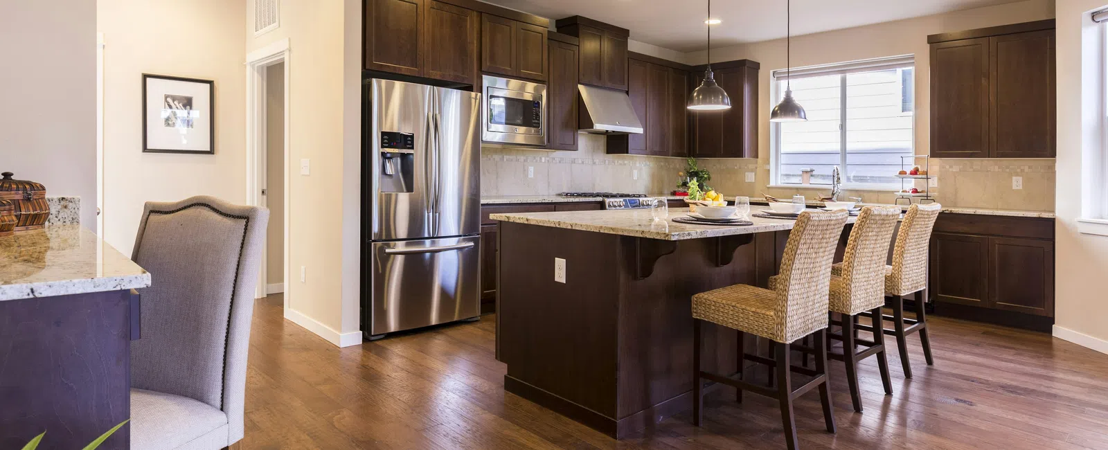 Spacious modern kitchen with dark wood cabinets, stainless steel appliances, island, and wicker bar stools under pendant lights.