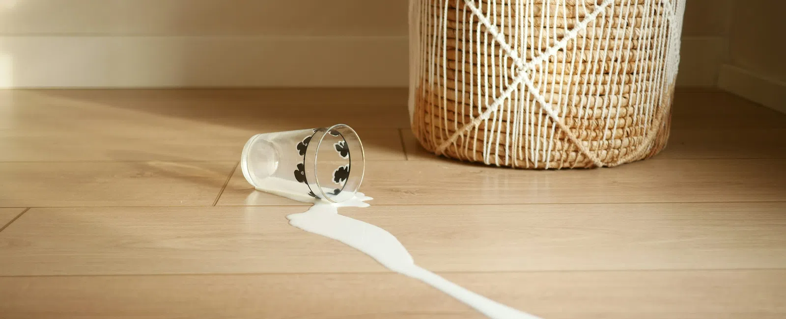 Spilled milk on wooden floor next to a woven basket with white string decoration.