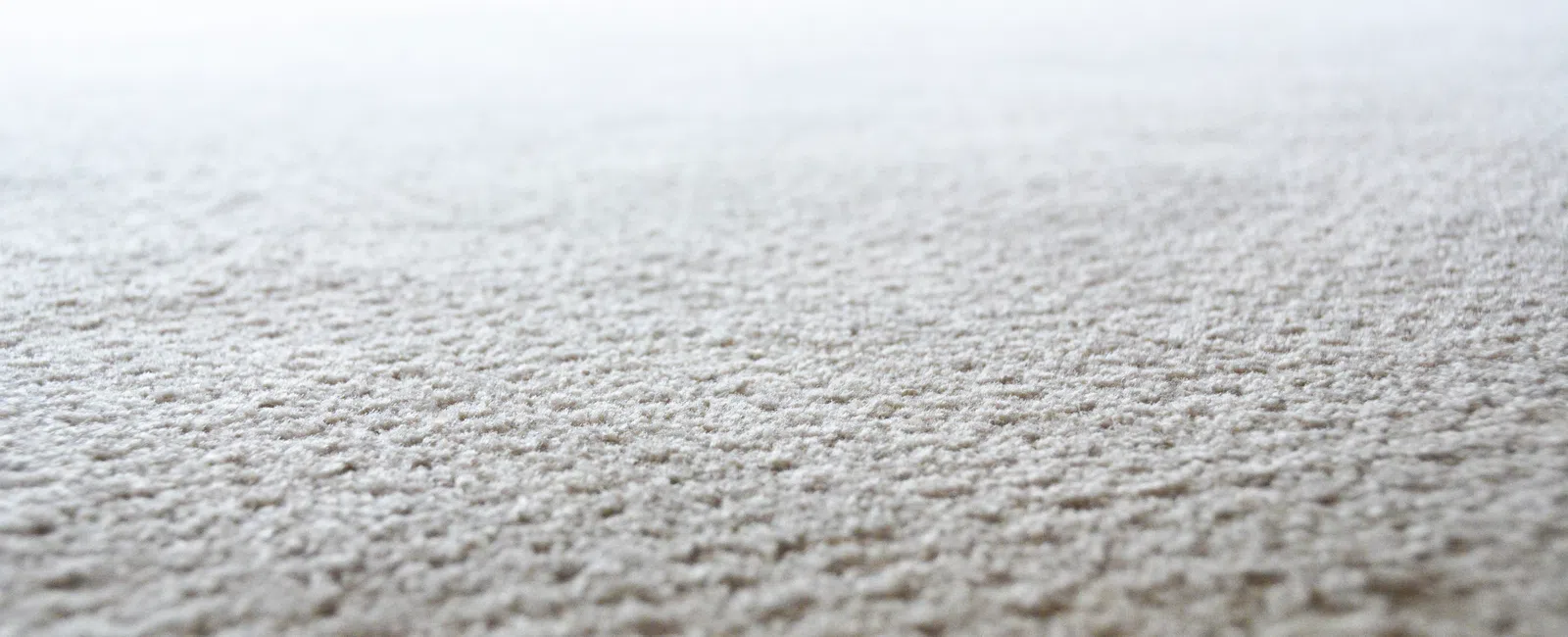 Close-up of a beige carpet texture with soft lighting in a room interior featuring wooden elements.