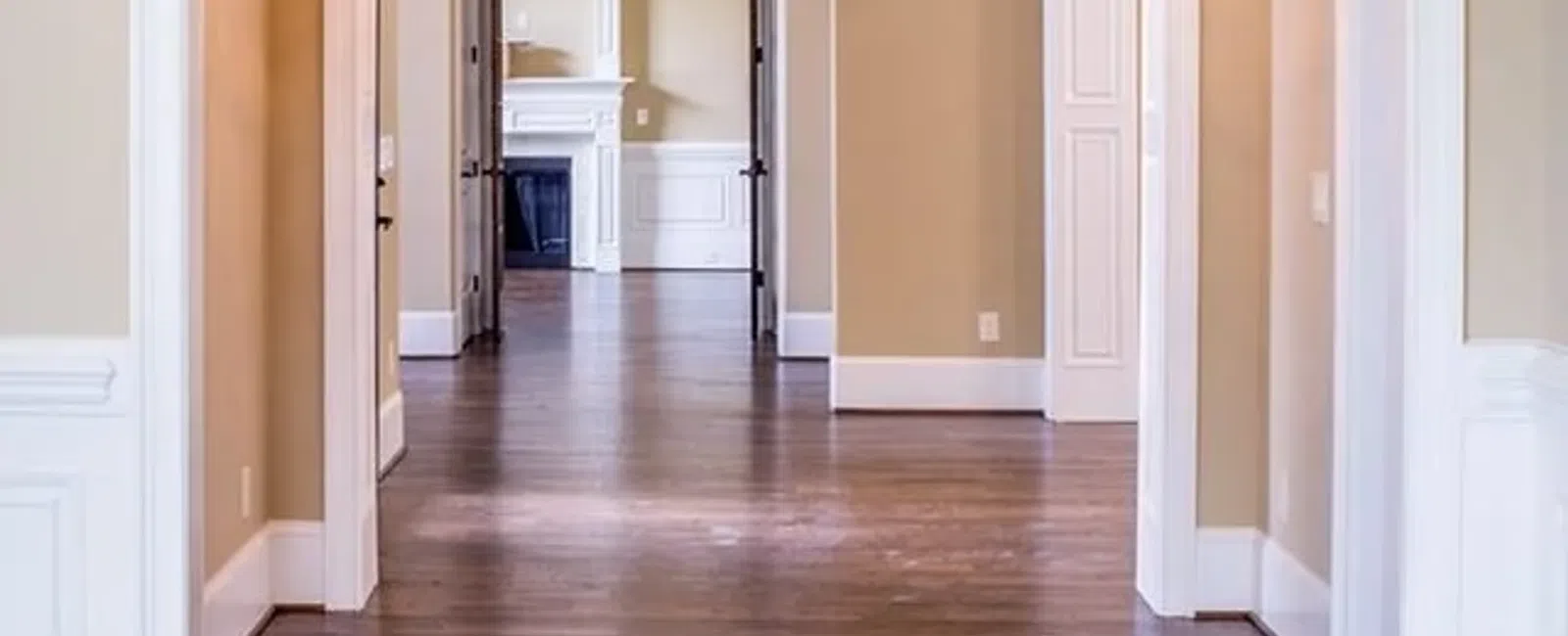 Spacious hallway with hardwood floors, beige walls, white trim, arched doorways, and chandelier lighting.