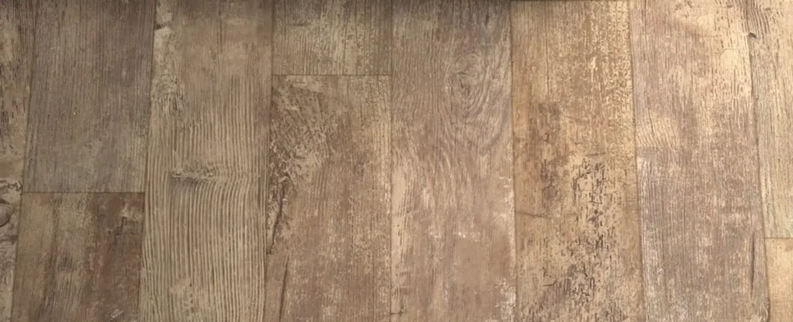 Close-up of rustic wooden floor panels with varied textures and tones beneath a wooden bench.