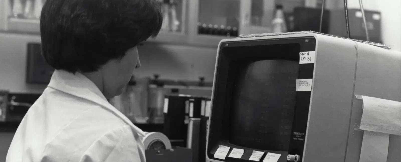 Woman in a lab coat working on a vintage computer showcasing aging IT technology in healthcare.