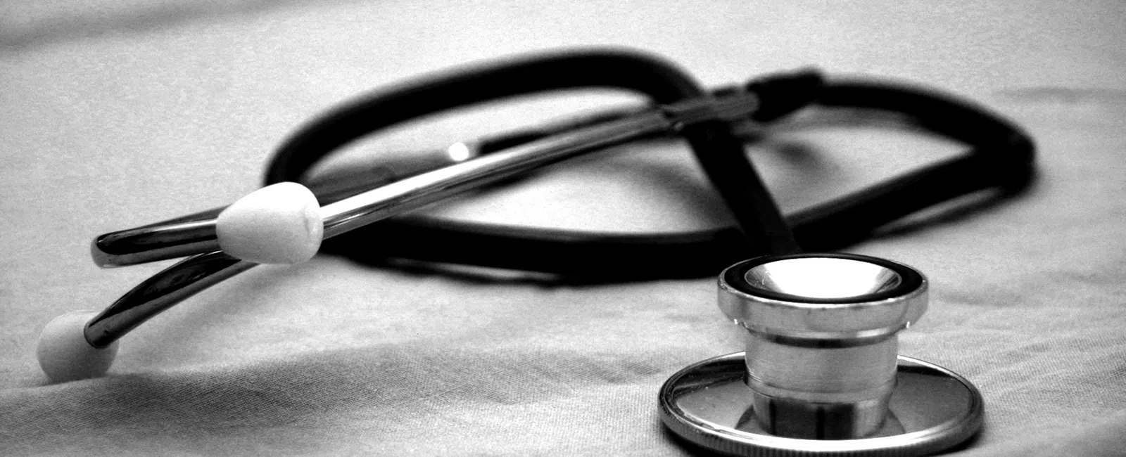 Black and white close-up of a stethoscope resting on a soft fabric surface, symbolizing healthcare.