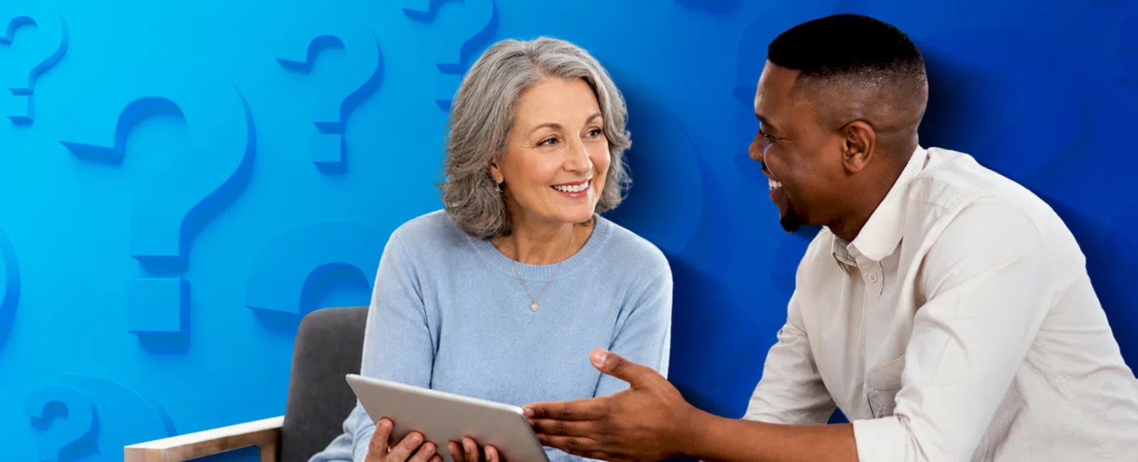 Senior woman and young man discussing and smiling while holding a digital tablet against a blue question mark background