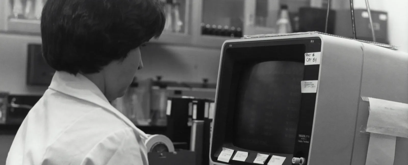 Woman in a lab coat working on a vintage computer showcasing aging IT technology in healthcare.