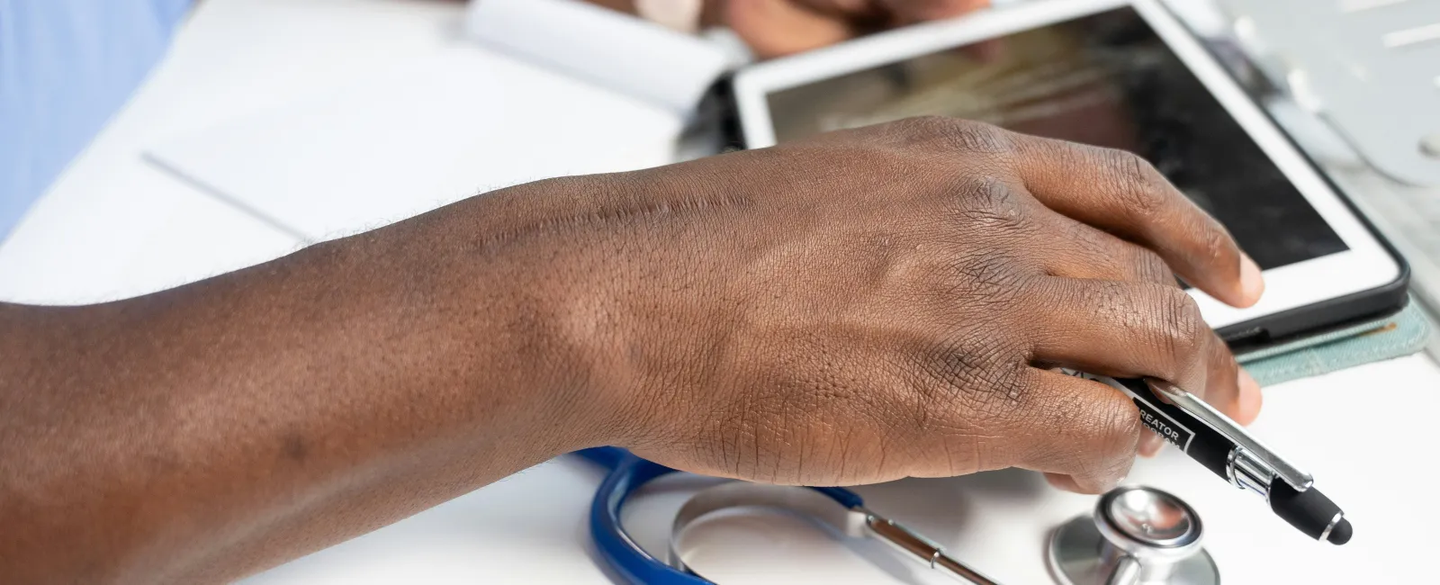 Close-up of a doctor’s hand using a digital tablet with a stethoscope showcasing the discussion of the IT gap in healthcare.