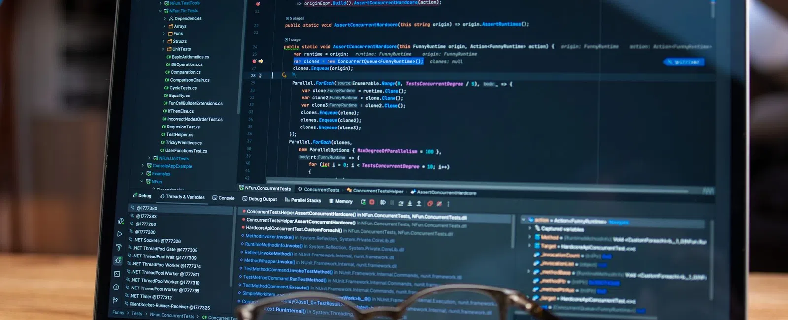 Open laptop displaying a software development environment with code and debugging tools, with glasses in front.