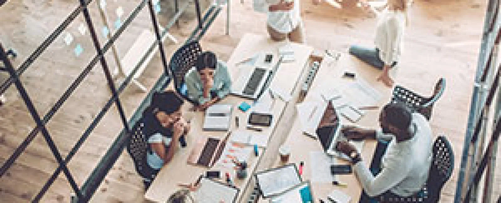 Overhead view of diverse team collaborating around a table with laptops, papers, and coffee in a modern office space