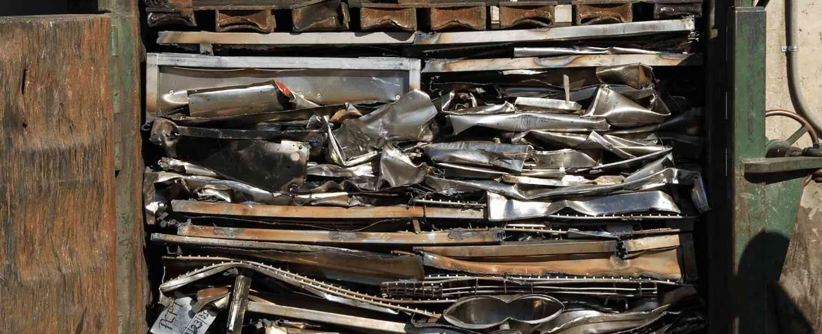 Metal scrap compacted tightly in an industrial baler machine for recycling purposes outdoors.