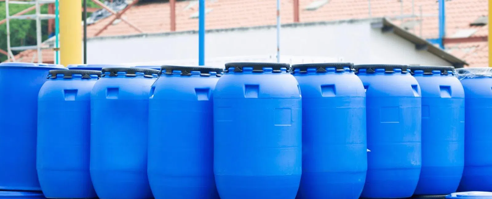 Stacked blue plastic barrels outdoors, used for storage or industrial purposes in a warehouse setting.